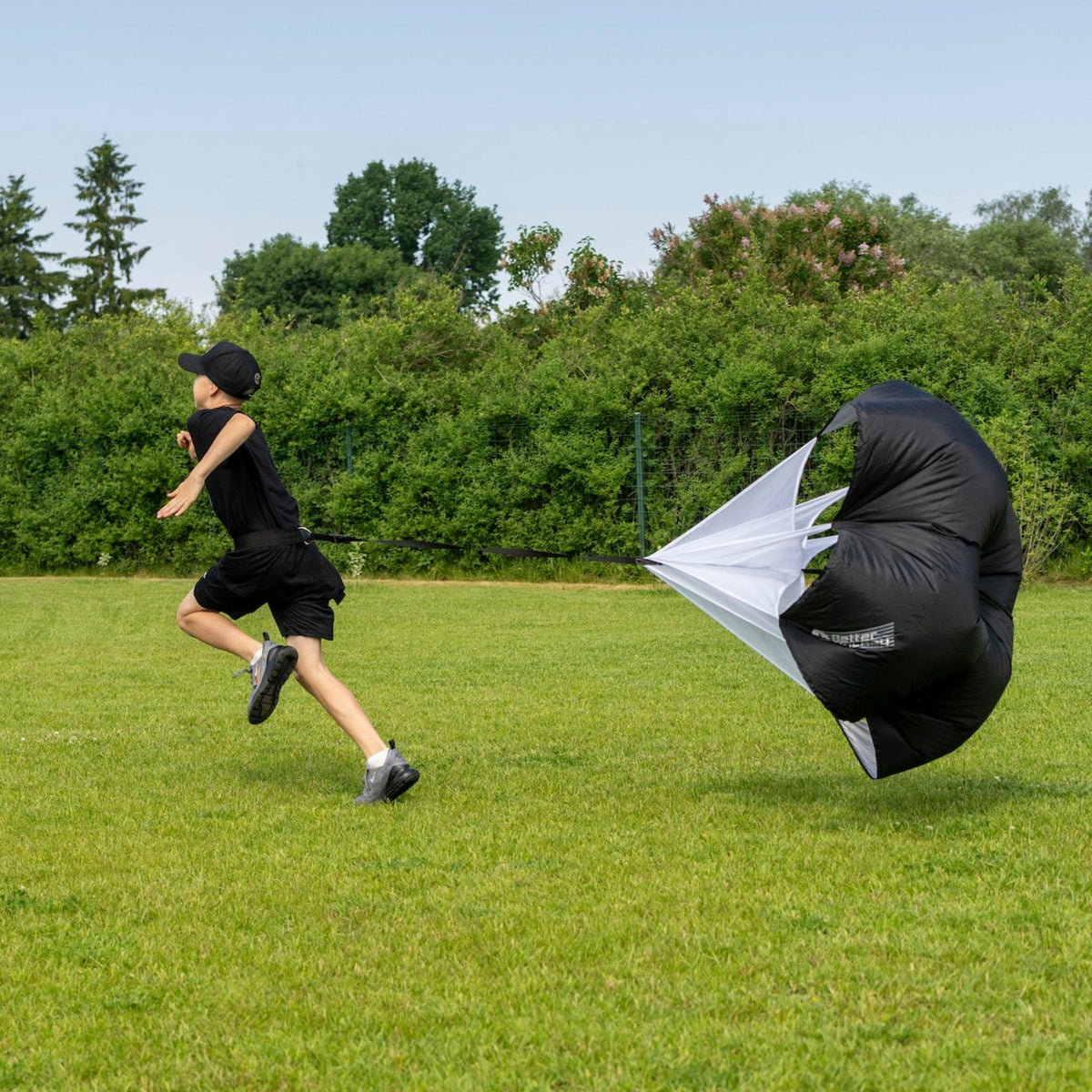 Young hockey player sprinting outdoors with a speed chute fully deployed, off-ice hockey speed training
