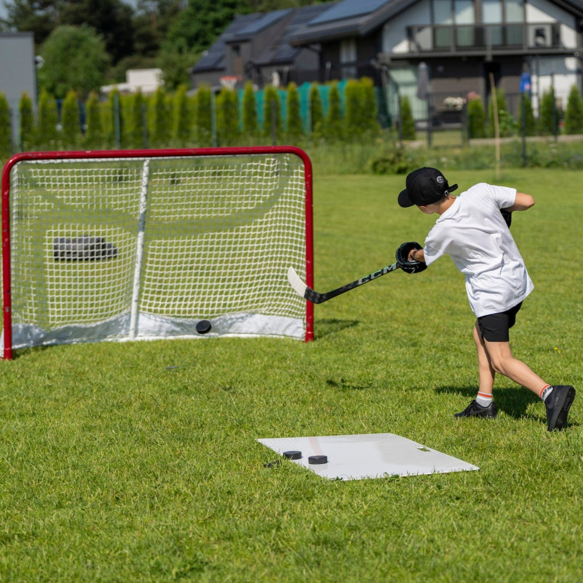 Young hockey player shooting puck on outdoor shooting pad in a backyard during warm-up