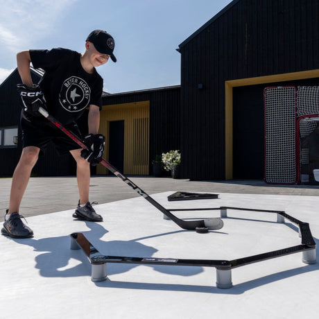 Young hockey player training stickhandling outdoors with the stickhandling trainer in a backyard
