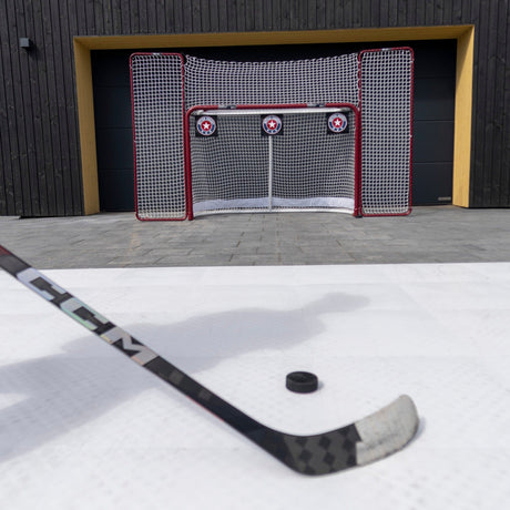 Hockey stick and puck on a shooting pad with shooting targets in a net in the driveway